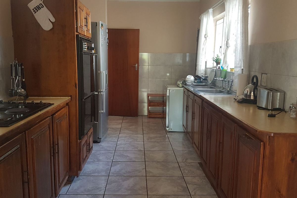 A functional galley-style kitchen featuring wooden cabinetry, an electric hob, built-in oven, and tiled finishes throughout.
