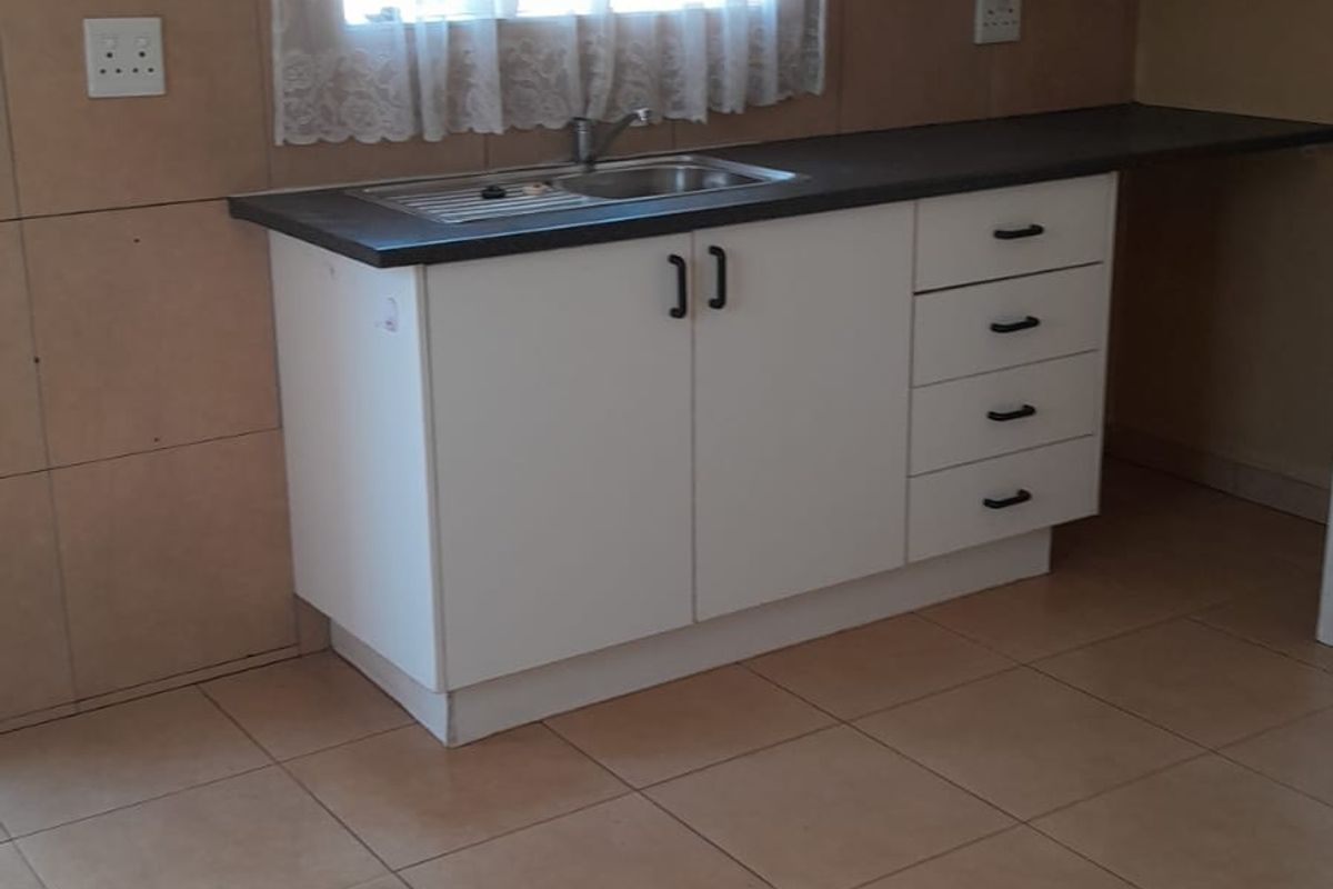 A functional kitchen area featuring white built-in cabinetry, a stainless steel sink, dark laminate countertops, and neutral tiled flooring.