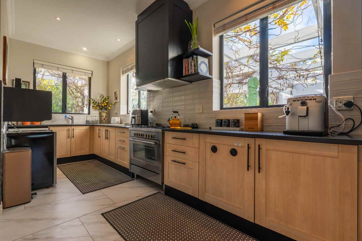 Modern kitchen featuring light wood cabinetry, dark countertops, stainless steel oven, extractor fan, and a tiled backsplash with ample natural light.