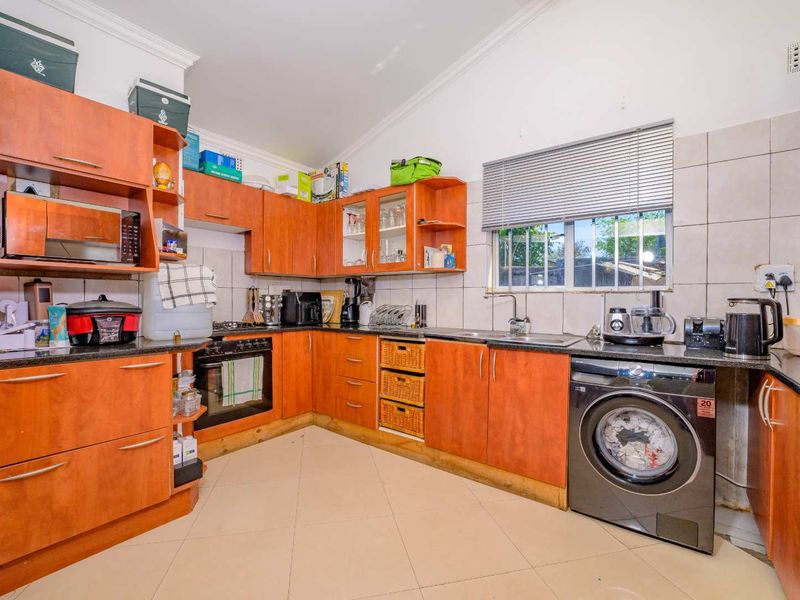 Functional kitchen featuring wood-tone cabinetry, laminate countertops, built-in oven, hob, and integrated laundry plumbing, offering a practical layout with tiled finishes.
