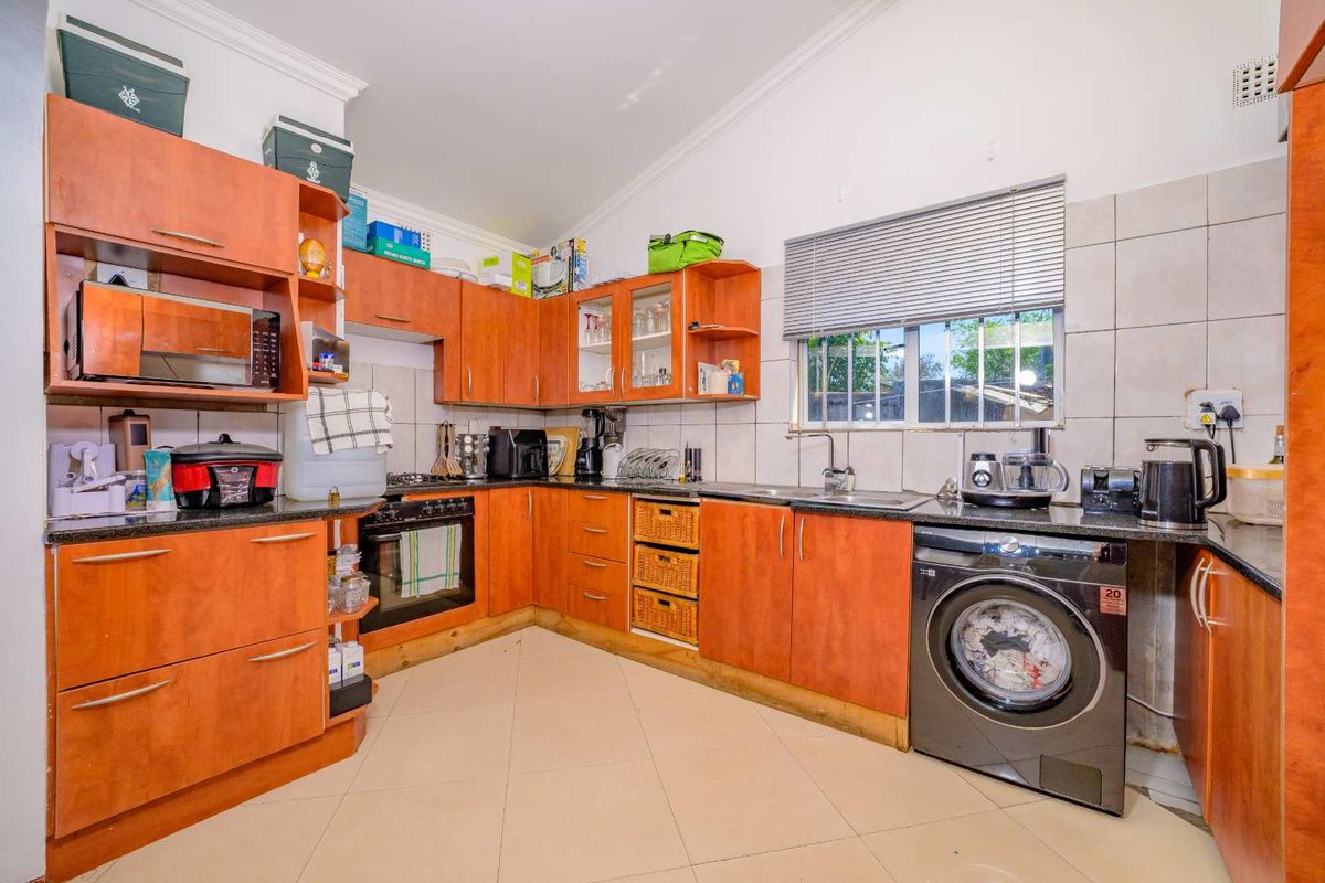 Functional kitchen featuring wood-tone cabinetry, laminate countertops, built-in oven, hob, and integrated laundry plumbing, offering a practical layout with tiled finishes.