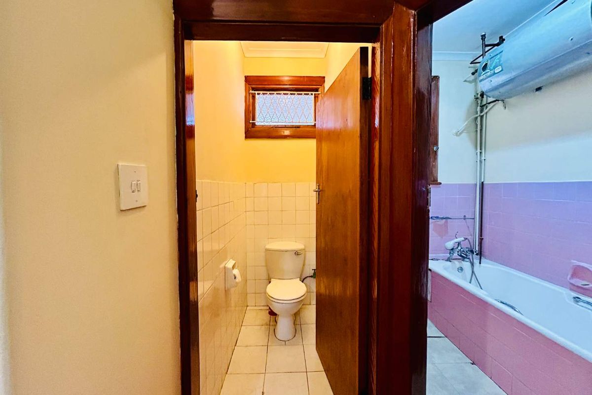 A dated bathroom featuring a separate toilet area and a bathtub with exposed plumbing and wall-mounted geyser.