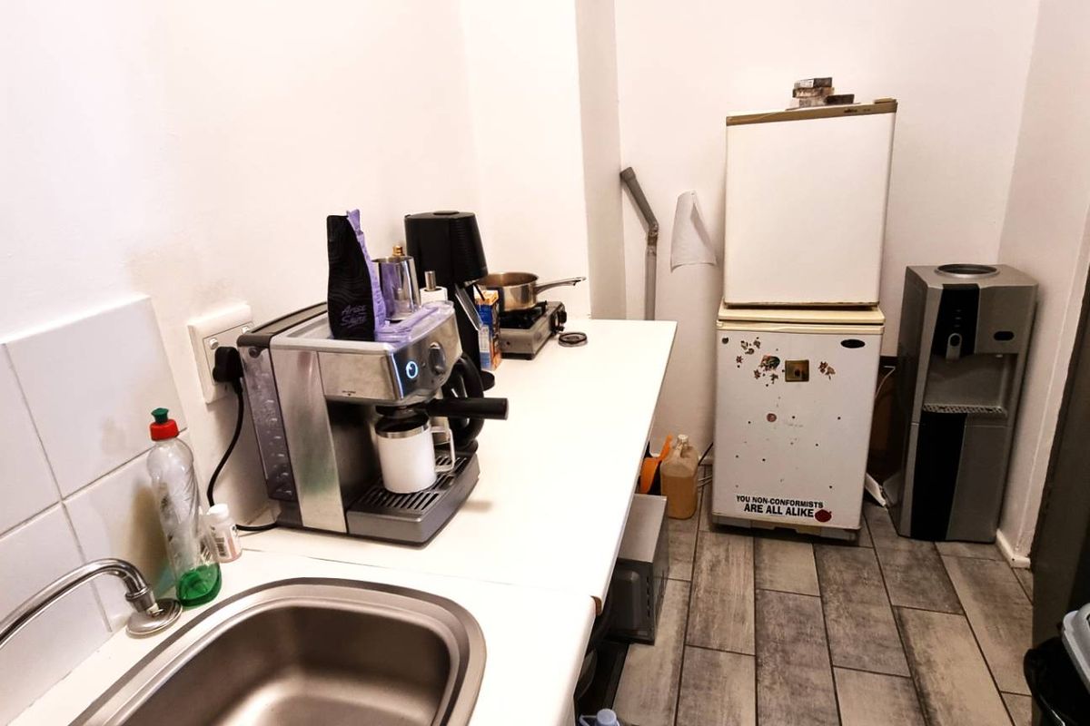 A compact office kitchenette featuring a stainless steel sink, tiled splashback, and basic counter space for beverage preparation.