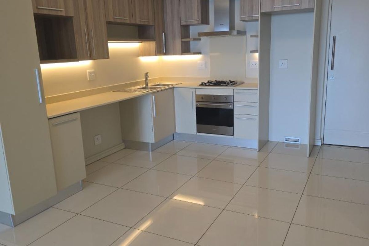 Modern open-plan kitchen featuring light wood cabinetry, stone countertops, integrated stainless steel oven, gas hob, and extractor fan with polished tile flooring.