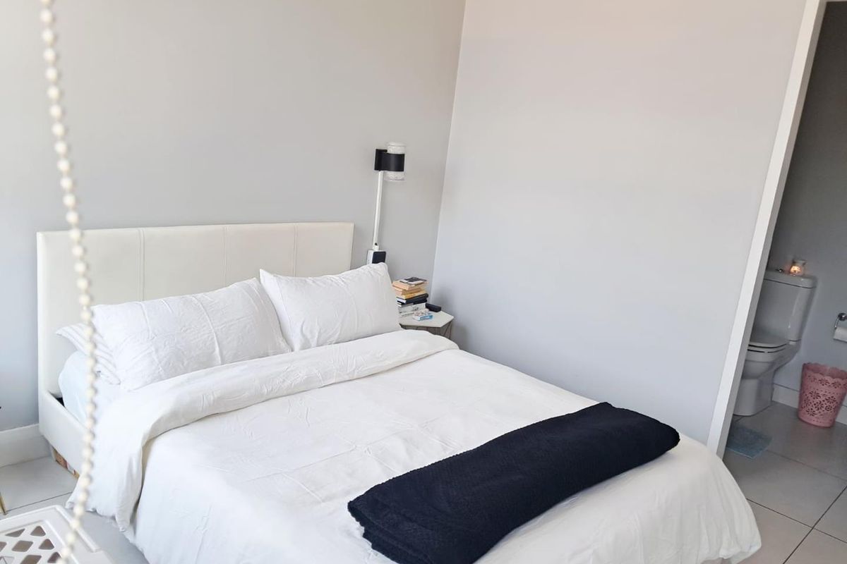 A bright bedroom featuring neutral walls and tiled flooring, with an adjoining en-suite bathroom visible through the doorway.