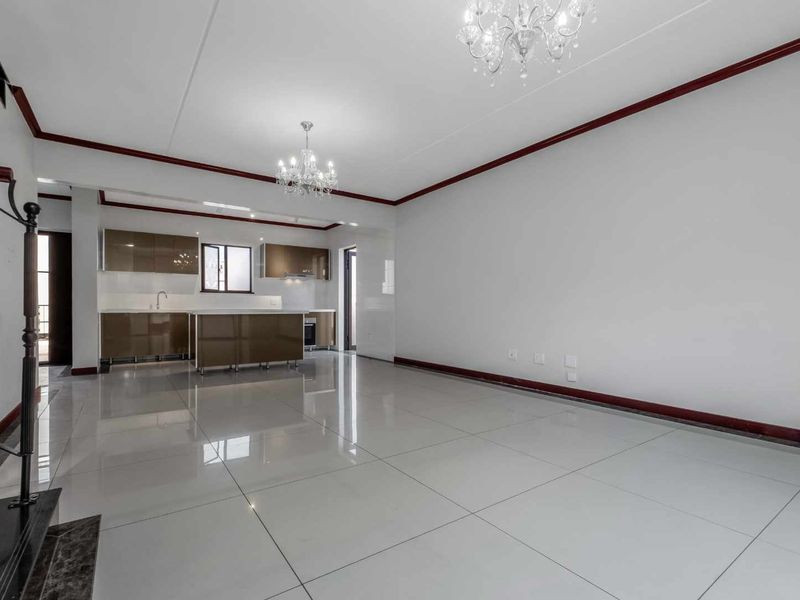 Spacious open-plan living and kitchen area featuring glossy tiled flooring, modern built-in cabinetry, a central kitchen island, and elegant chandelier lighting.