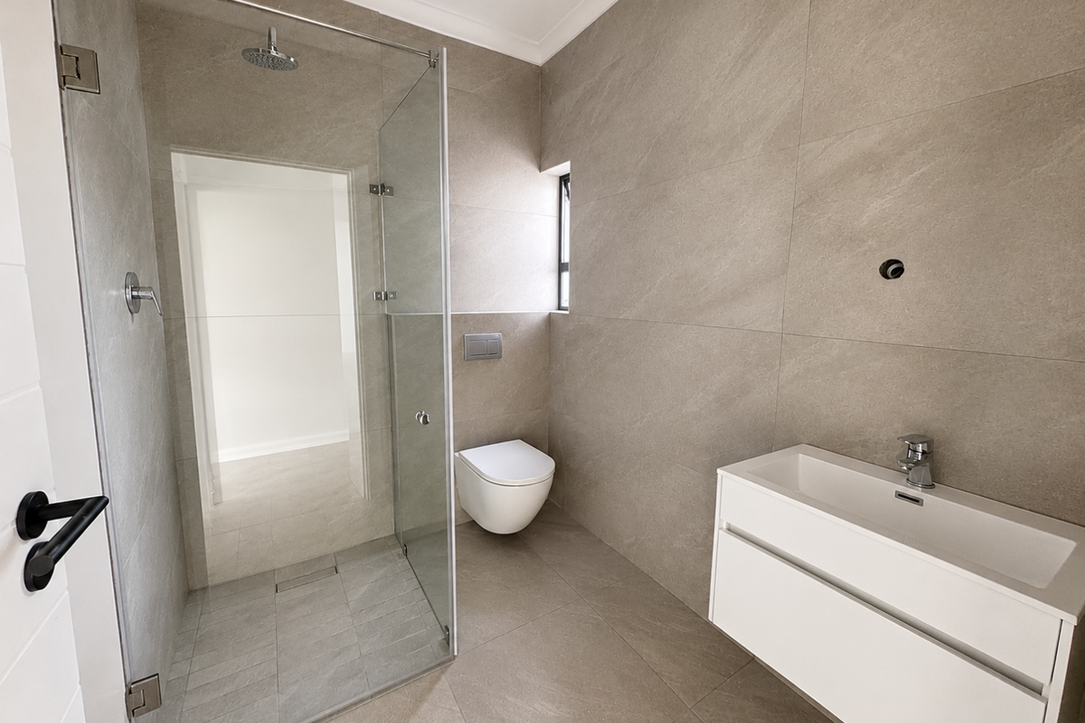 Modern bathroom featuring a frameless glass walk-in shower, wall-mounted toilet, and a sleek floating vanity with integrated basin.