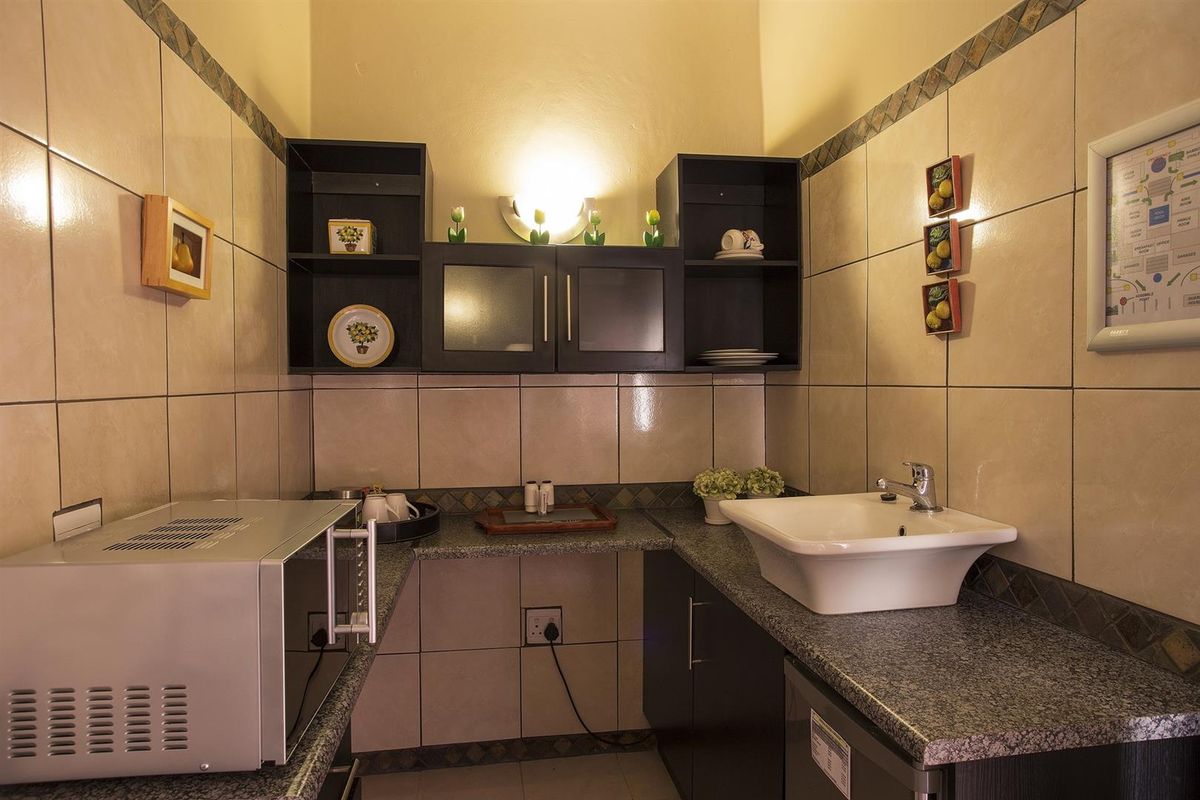 A compact kitchenette featuring granite countertops, built-in cabinetry, wall-mounted shelving, and a ceramic-tiled backsplash with a fitted basin.