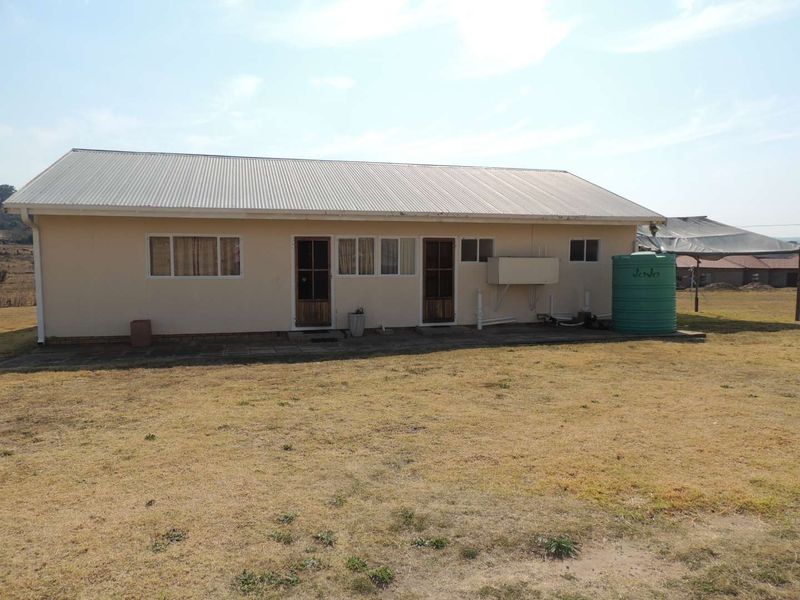 Rear view of a single-story house featuring a corrugated metal roof, paved walkway, and an external water storage tank.