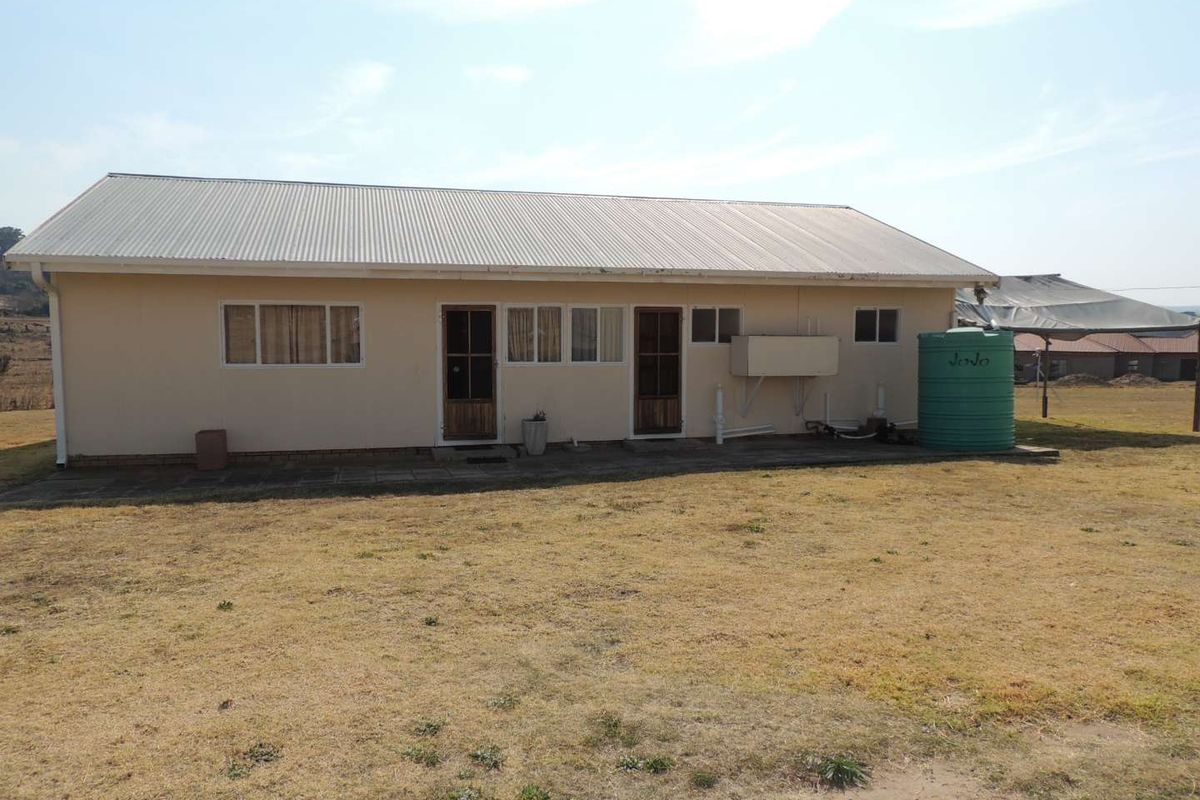Rear view of a single-story house featuring a corrugated metal roof, paved walkway, and an external water storage tank.