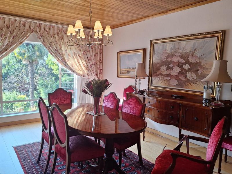 A formal dining room featuring a timber-paneled ceiling, a classic chandelier, and a large window providing natural light and garden views.