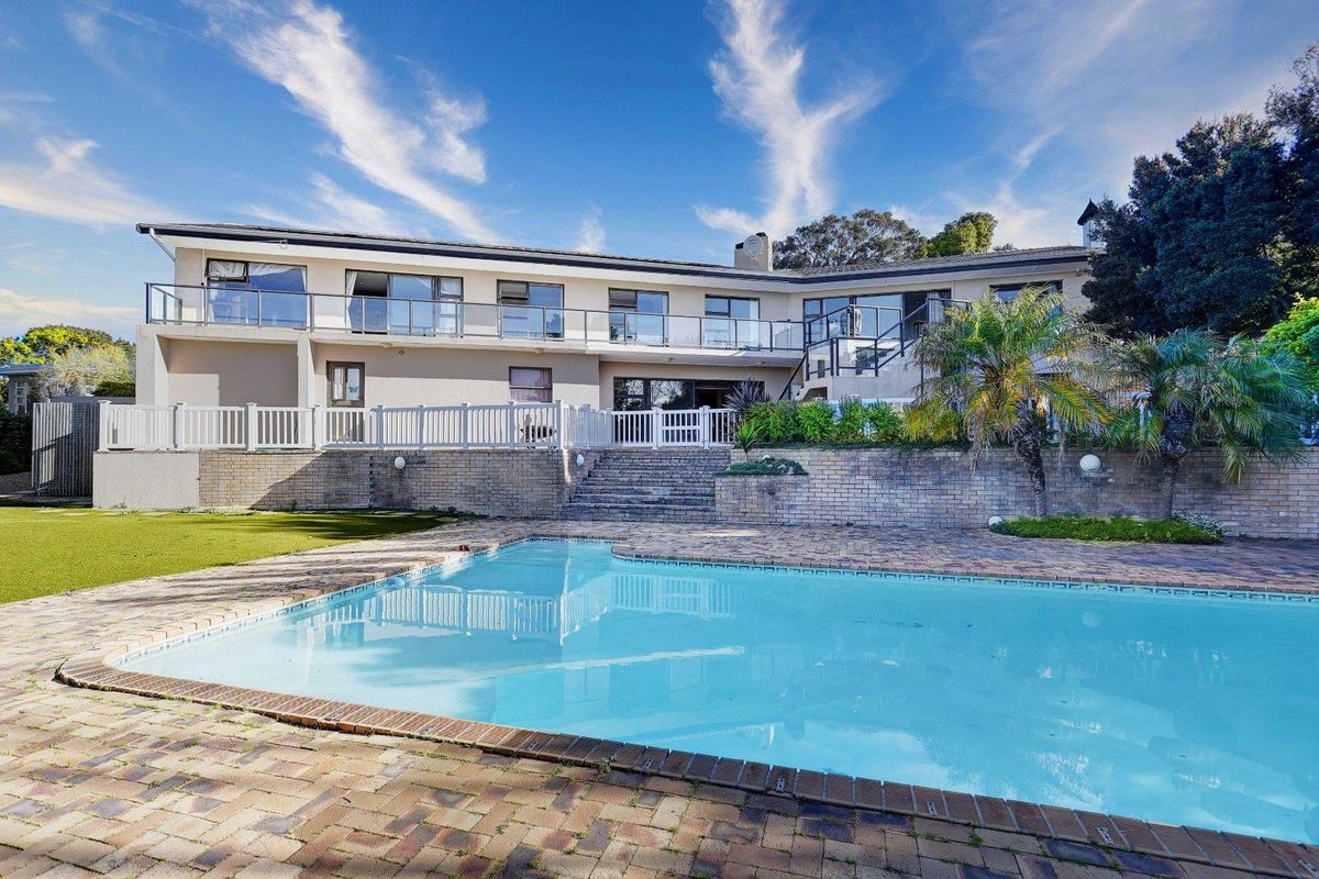 Rear view of the property featuring a swimming pool, brick paved patio area, and a spacious upper-level balcony with glass balustrades.
