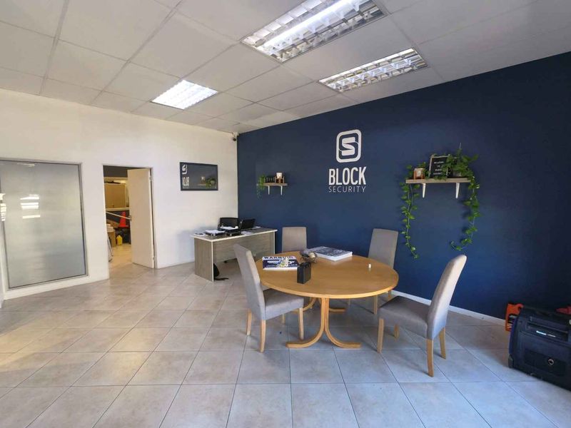 A professional office space featuring tiled flooring, a suspended ceiling with recessed lighting, and a prominent feature wall with branding.