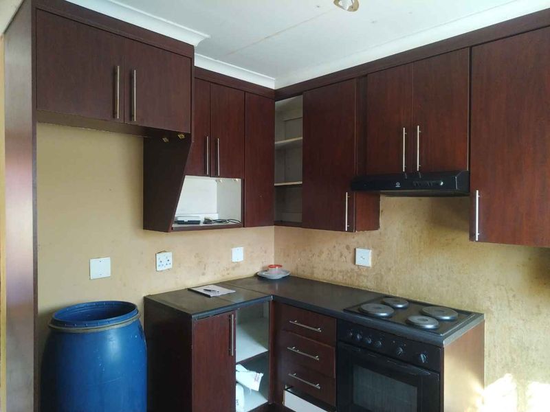 A kitchen featuring dark wood cabinetry, laminate countertops, and built-in cooking appliances. The space requires cosmetic updates to the wall finishes and cabinetry.
