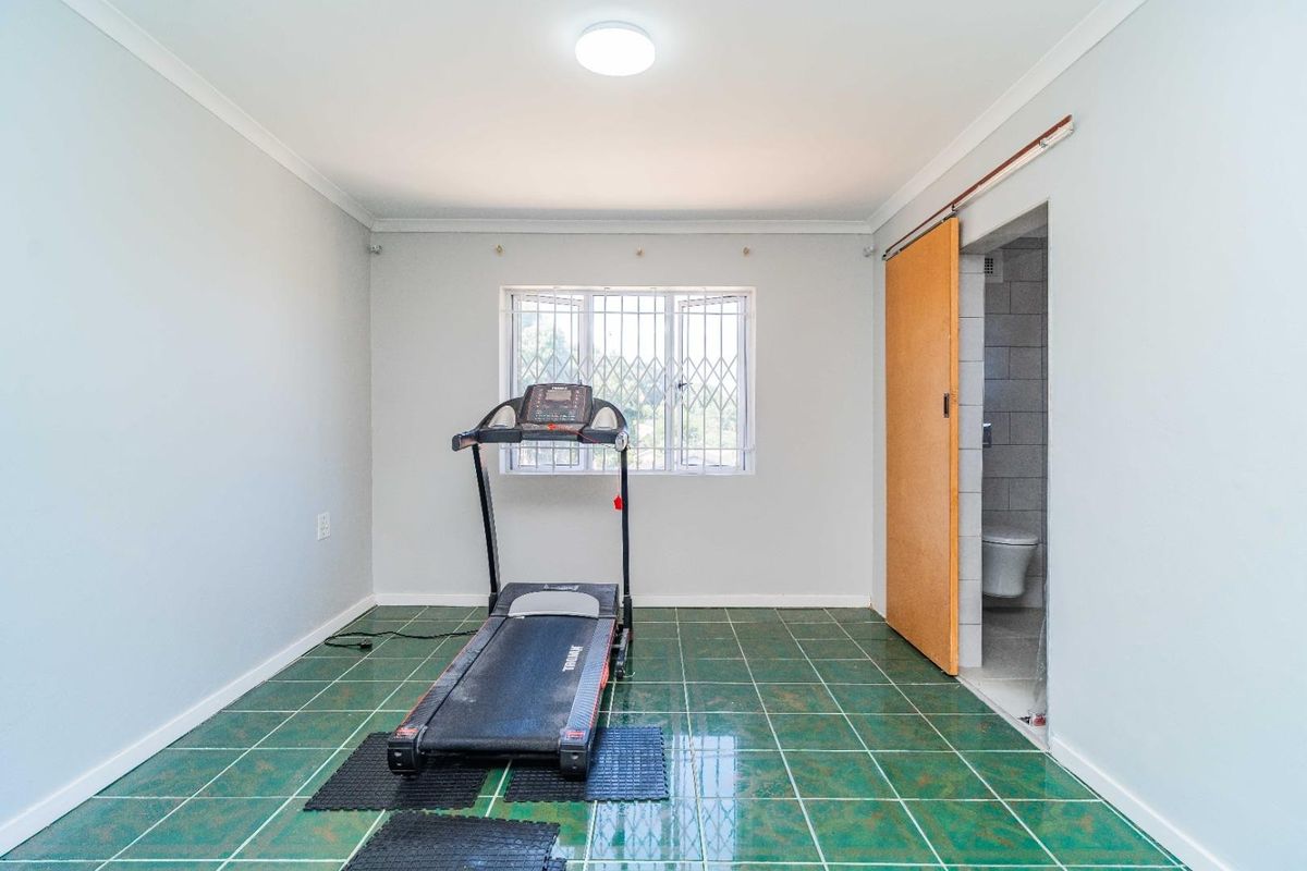 A bedroom featuring green tiled flooring, security bars on the window, and an en-suite bathroom accessed via a sliding door.