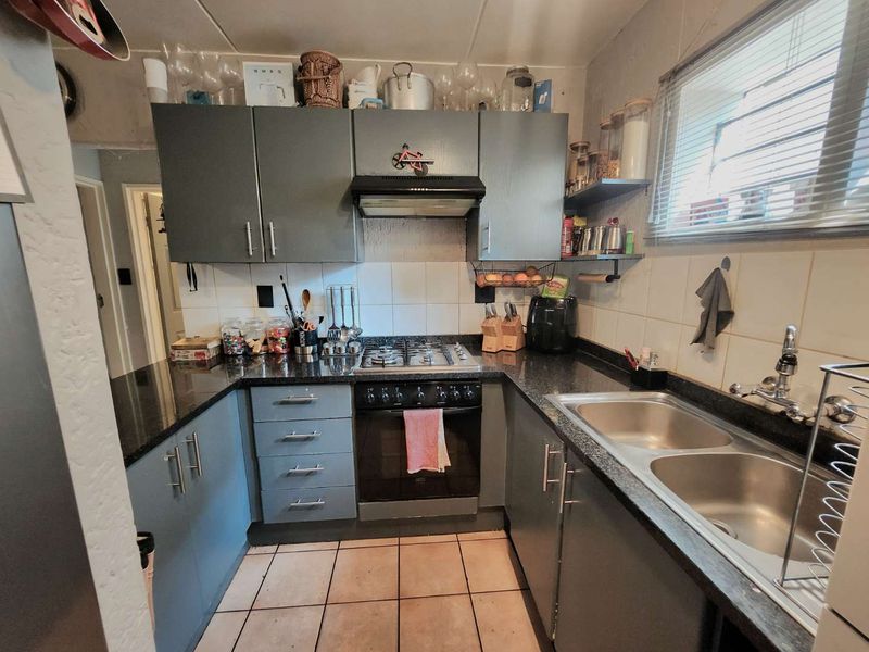 Compact kitchen featuring dark grey cabinetry, granite countertops, a gas hob with extractor fan, and a double stainless steel sink.