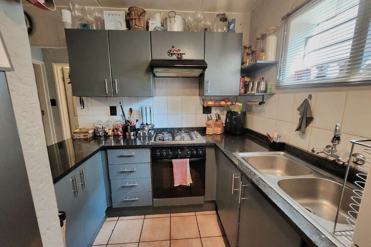 Compact kitchen featuring dark grey cabinetry, granite countertops, a gas hob with extractor fan, and a double stainless steel sink.