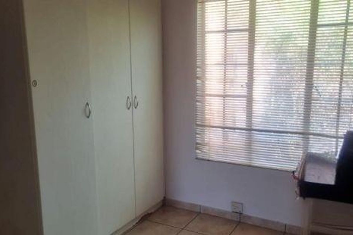 A bedroom featuring built-in wardrobes, tiled flooring, and a window fitted with horizontal blinds.