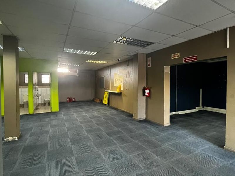 Open plan commercial office space featuring suspended ceiling grid, recessed fluorescent lighting, and integrated restroom facilities.