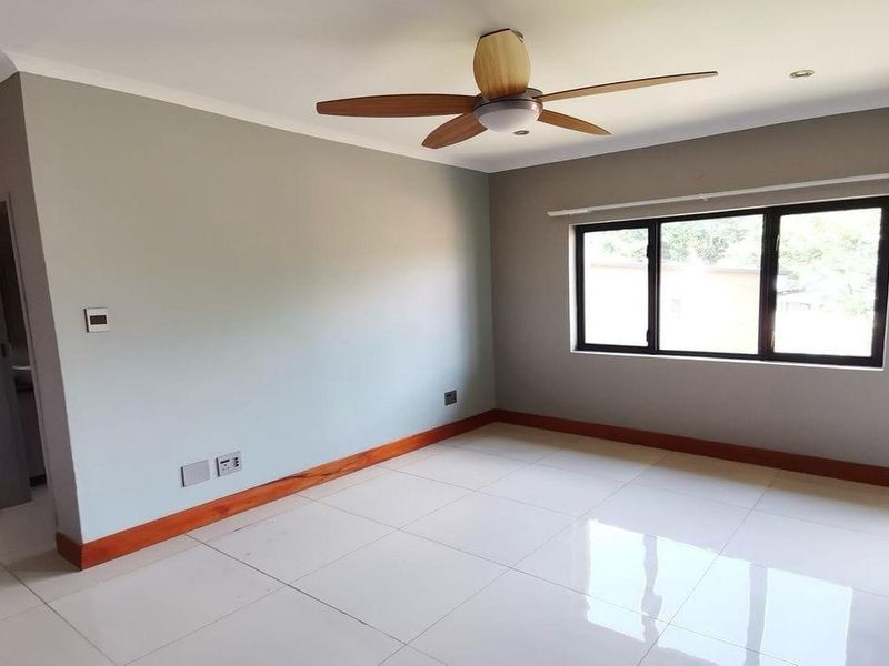 A bright, empty bedroom featuring neutral walls, large windows, tiled flooring, and a ceiling fan, offering a clean canvas for personalization.