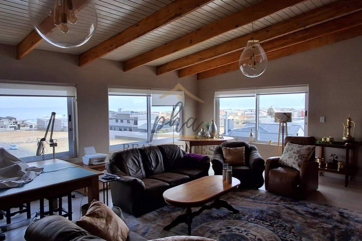 Spacious living room featuring exposed timber ceiling beams, large windows with coastal views, and a built-in wood-burning fireplace.