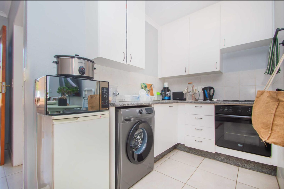 Compact kitchen featuring white cabinetry, granite countertops, tiled backsplash, and built-in oven with hob, providing a functional and efficient workspace.