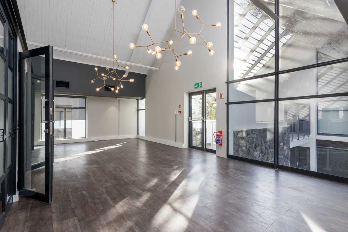 Spacious, modern office area featuring high vaulted ceilings, timber-look flooring, and expansive windows providing abundant natural light.