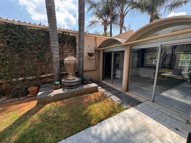 Rear exterior view featuring a paved patio area, sliding glass doors, and a decorative stone fountain set against a landscaped garden wall.