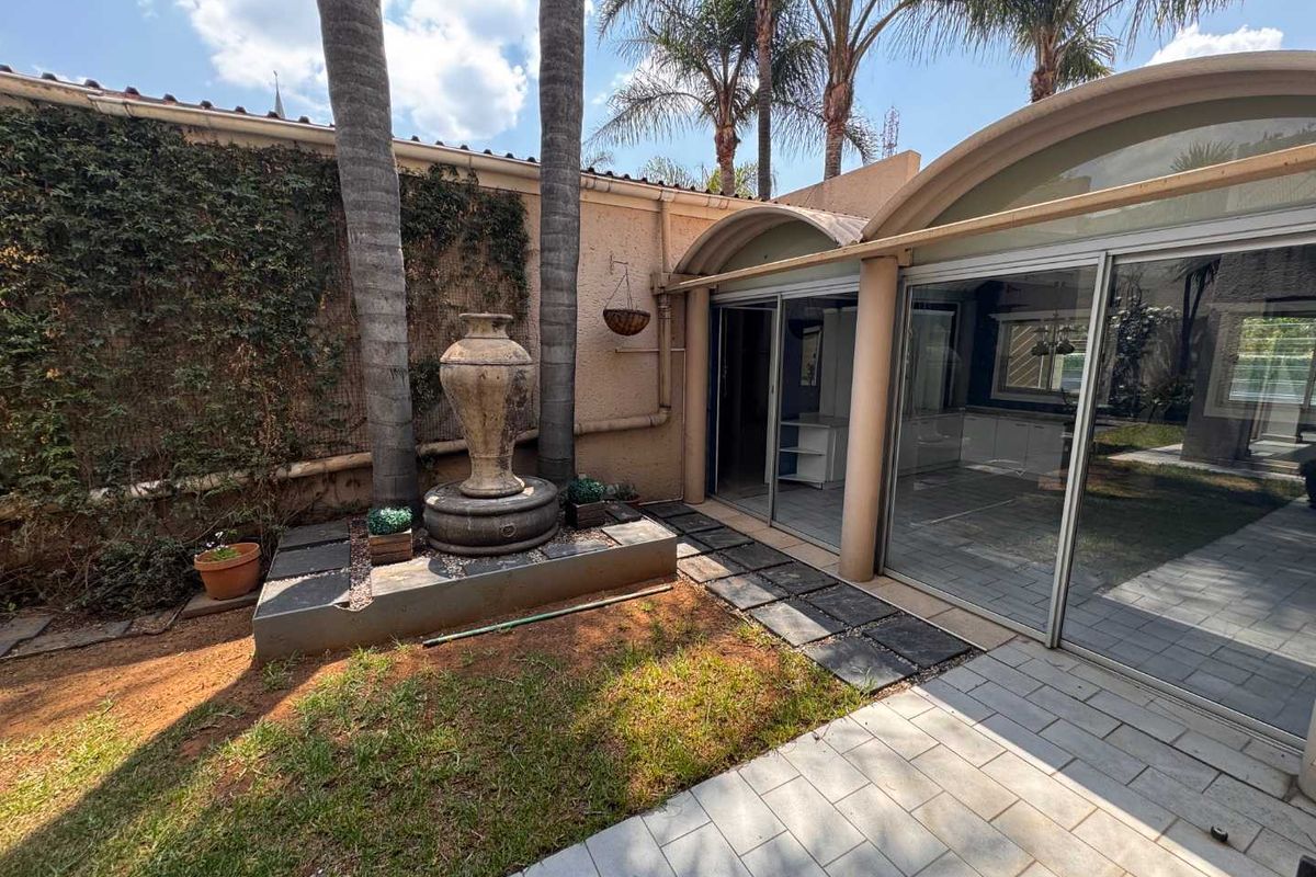 Rear exterior view featuring a paved patio area, sliding glass doors, and a decorative stone fountain set against a landscaped garden wall.
