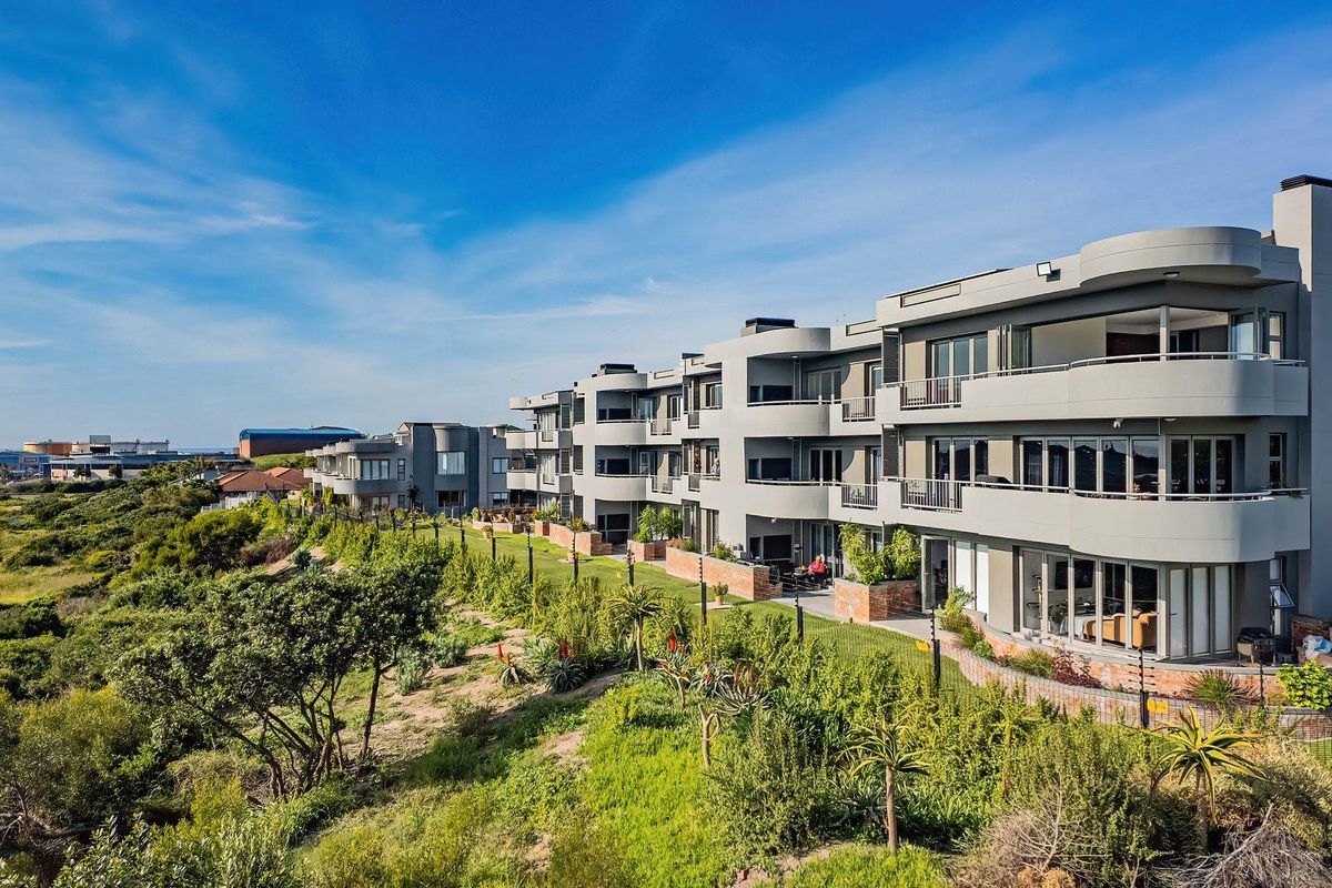 Aerial view of the apartment complex rear elevation, featuring private balconies, sliding glass doors, and landscaped garden areas.