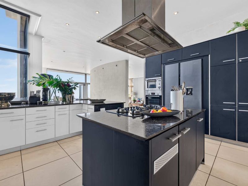 Modern kitchen featuring a central island with gas cooktop, stainless steel extractor fan, built-in appliances, and sleek dark and white cabinetry.