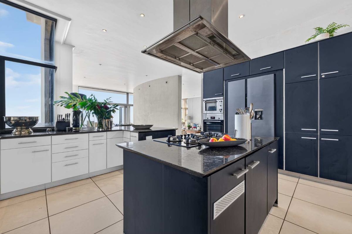 Modern kitchen featuring a central island with gas cooktop, stainless steel extractor fan, built-in appliances, and sleek dark and white cabinetry.