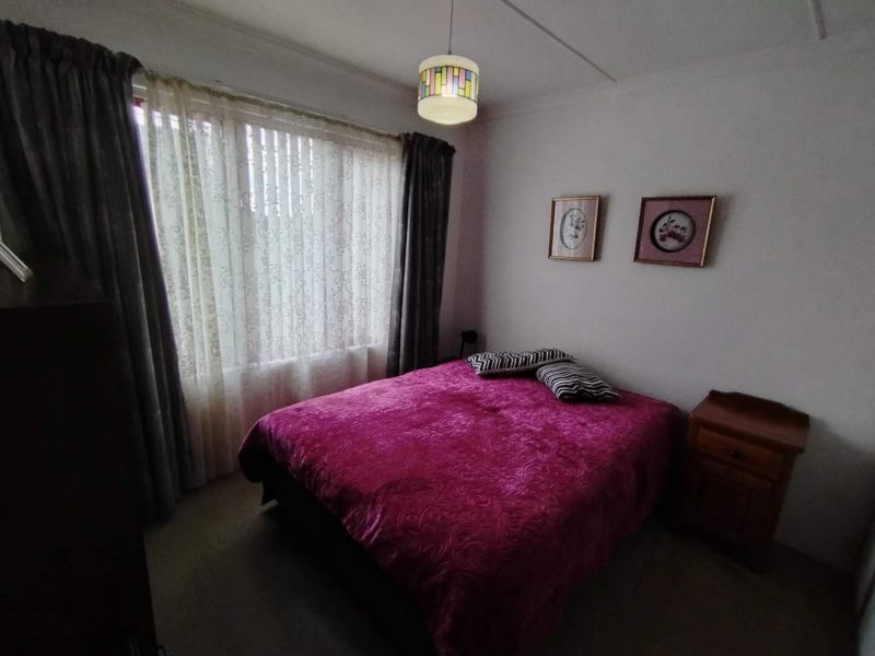 A standard bedroom featuring a large window with curtains and a central ceiling light fixture.