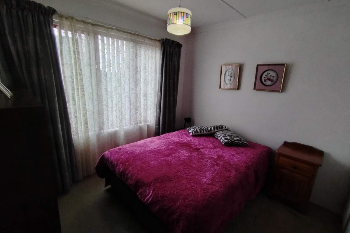 A standard bedroom featuring a large window with curtains and a central ceiling light fixture.