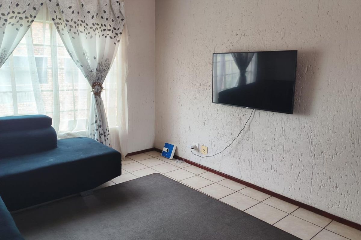 A living room featuring tiled flooring and textured wall finishes, equipped with a wall-mounted television and large window with natural light.