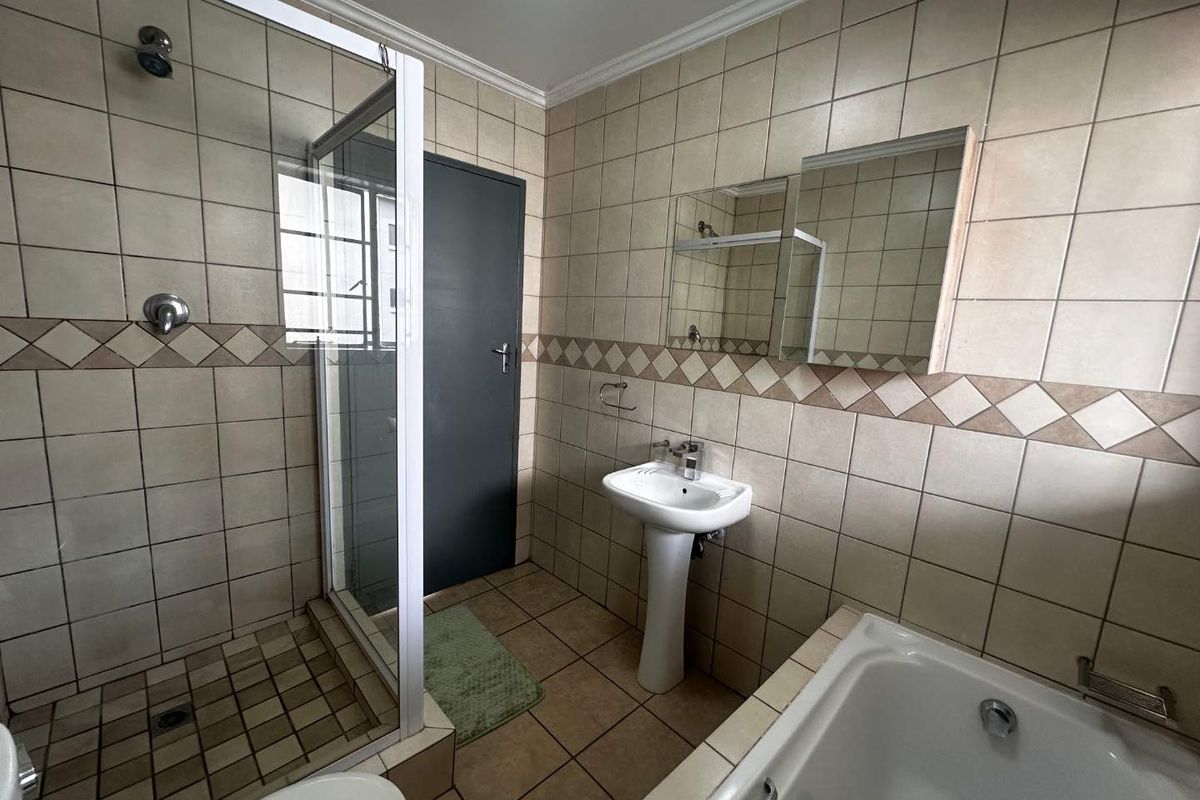 A functional bathroom featuring a separate shower enclosure, a pedestal basin, and a bathtub with neutral wall and floor tiling.