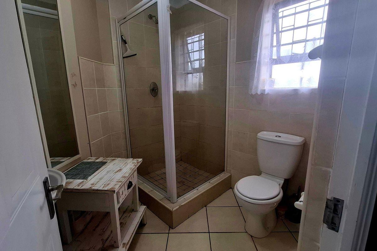A functional bathroom featuring a corner shower enclosure, tiled walls and flooring, and a standard toilet.