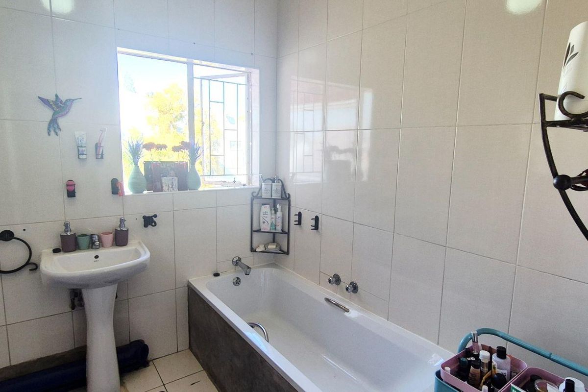 A functional bathroom featuring a pedestal basin, a standard bathtub with wall-mounted fixtures, and full-height wall tiling.