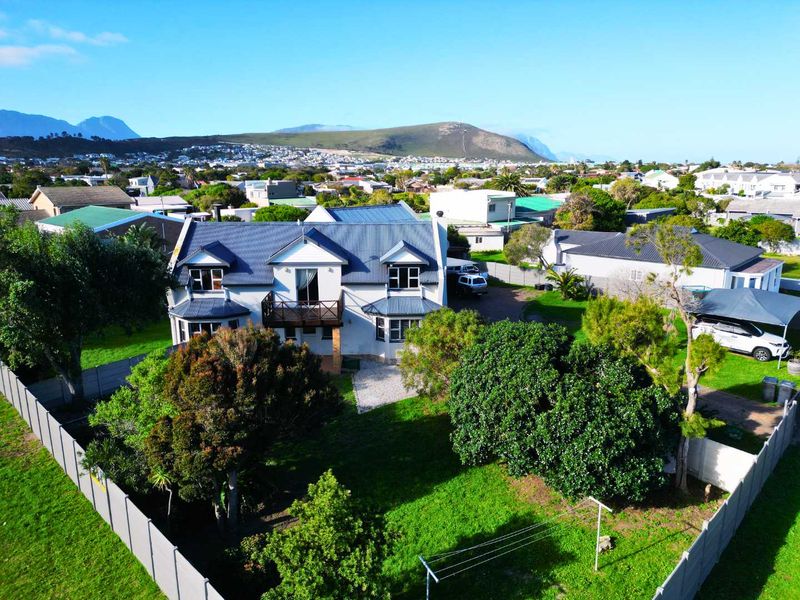 Aerial view of a residential property featuring a multi-level house with a metal roof, balcony, and surrounding garden area in a suburban setting.