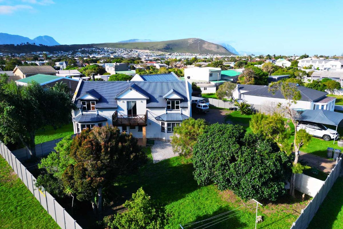 Aerial view of a residential property featuring a multi-level house with a metal roof, balcony, and surrounding garden area in a suburban setting.