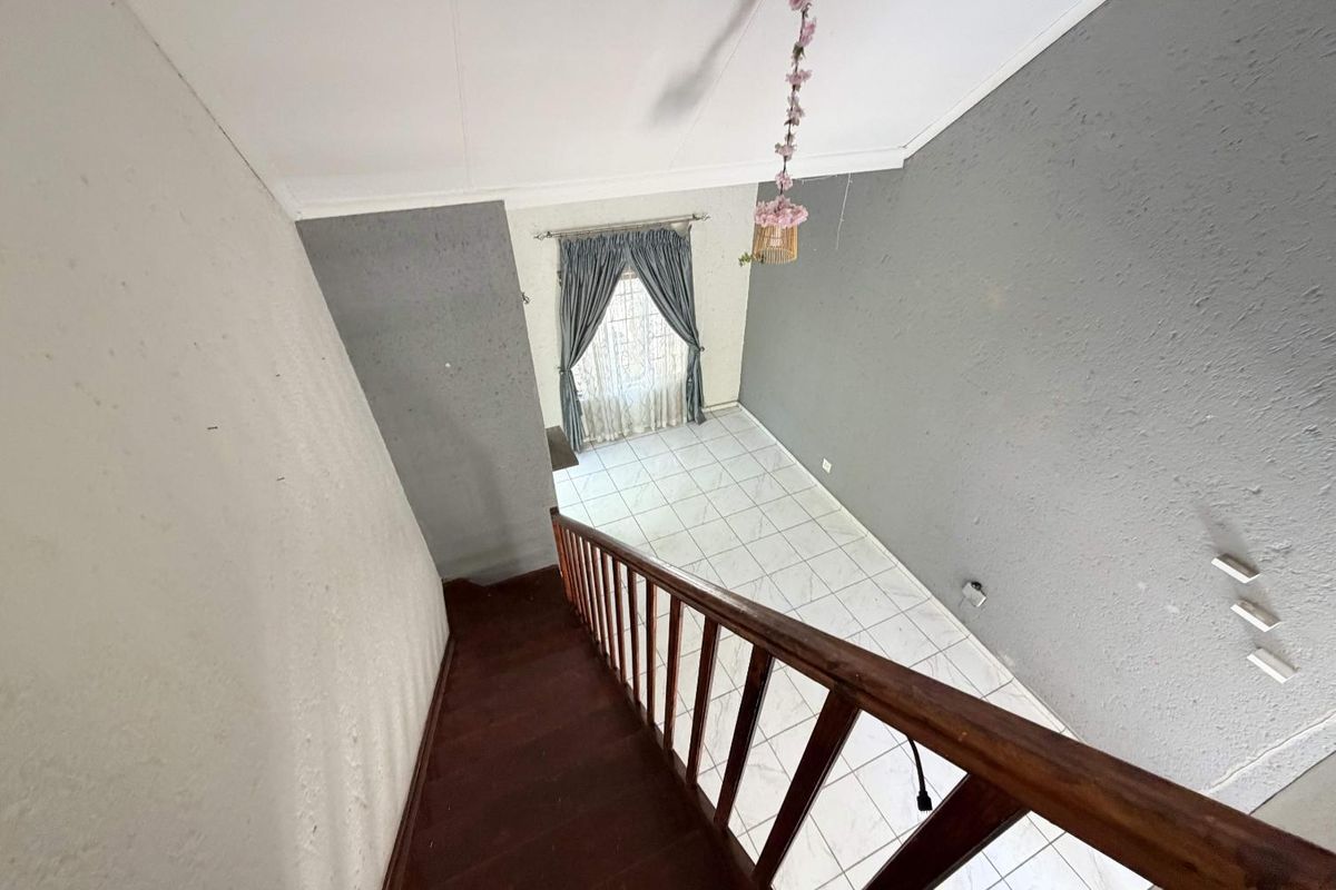 A view looking down a wooden staircase into a tiled living area with grey accent walls and a window with curtains.
