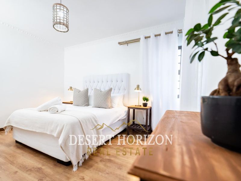 A bright and well-maintained bedroom featuring laminate flooring and decorative crown molding.