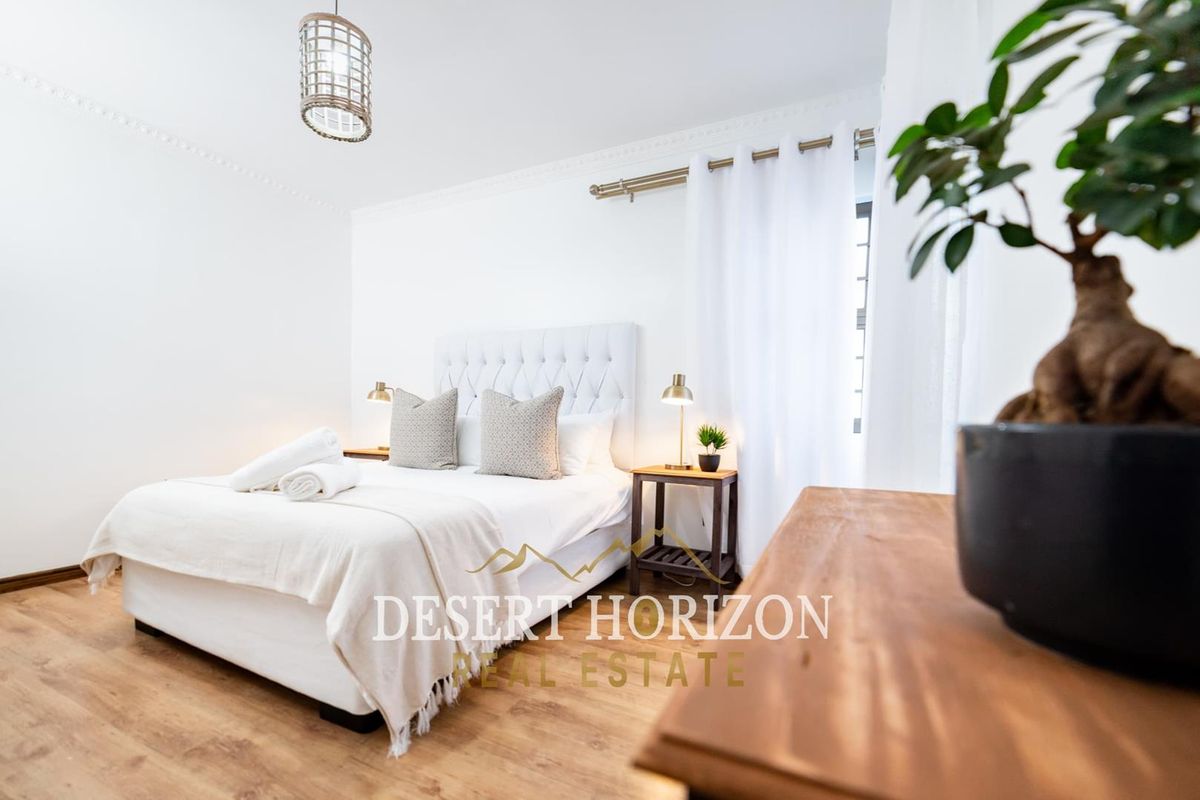 A bright and well-maintained bedroom featuring laminate flooring and decorative crown molding.