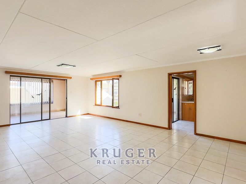 Spacious, light-filled living area featuring neutral tiled flooring, large windows, and a sliding door leading to an outdoor space.