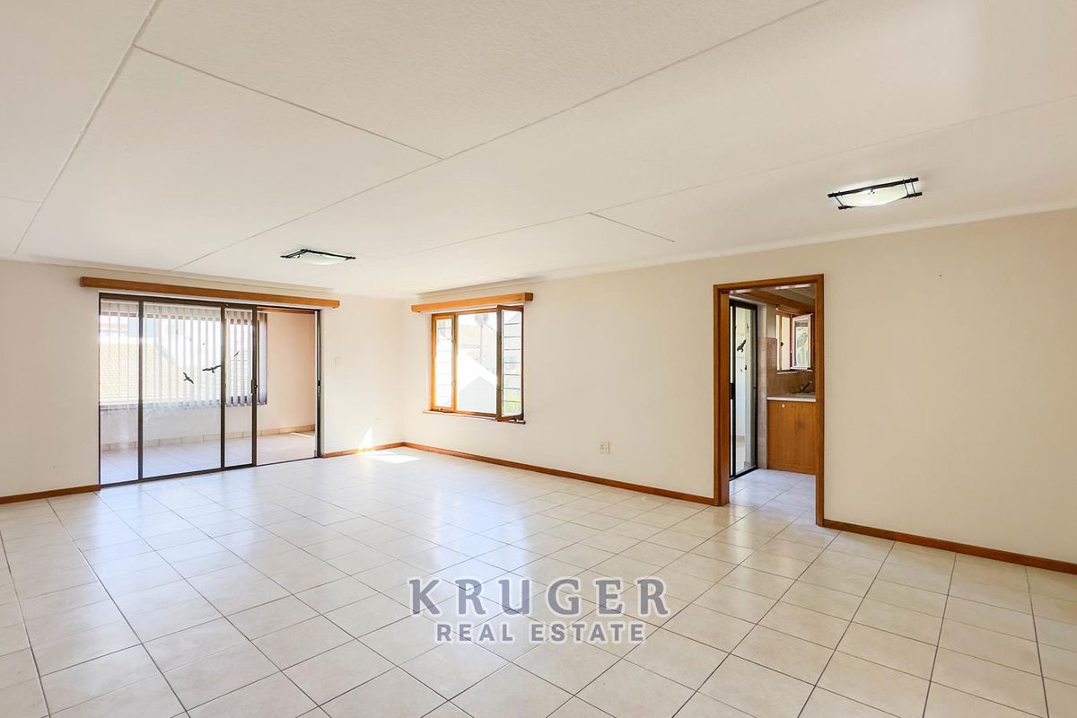 Spacious, light-filled living area featuring neutral tiled flooring, large windows, and a sliding door leading to an outdoor space.