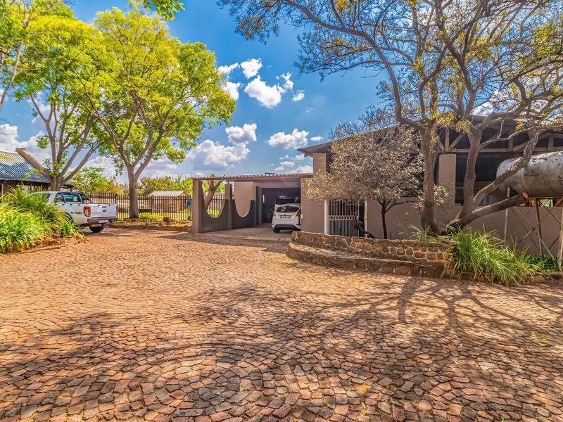 Front exterior view of the farm property featuring a cobblestone driveway, carport, and established trees with a large water storage tank.