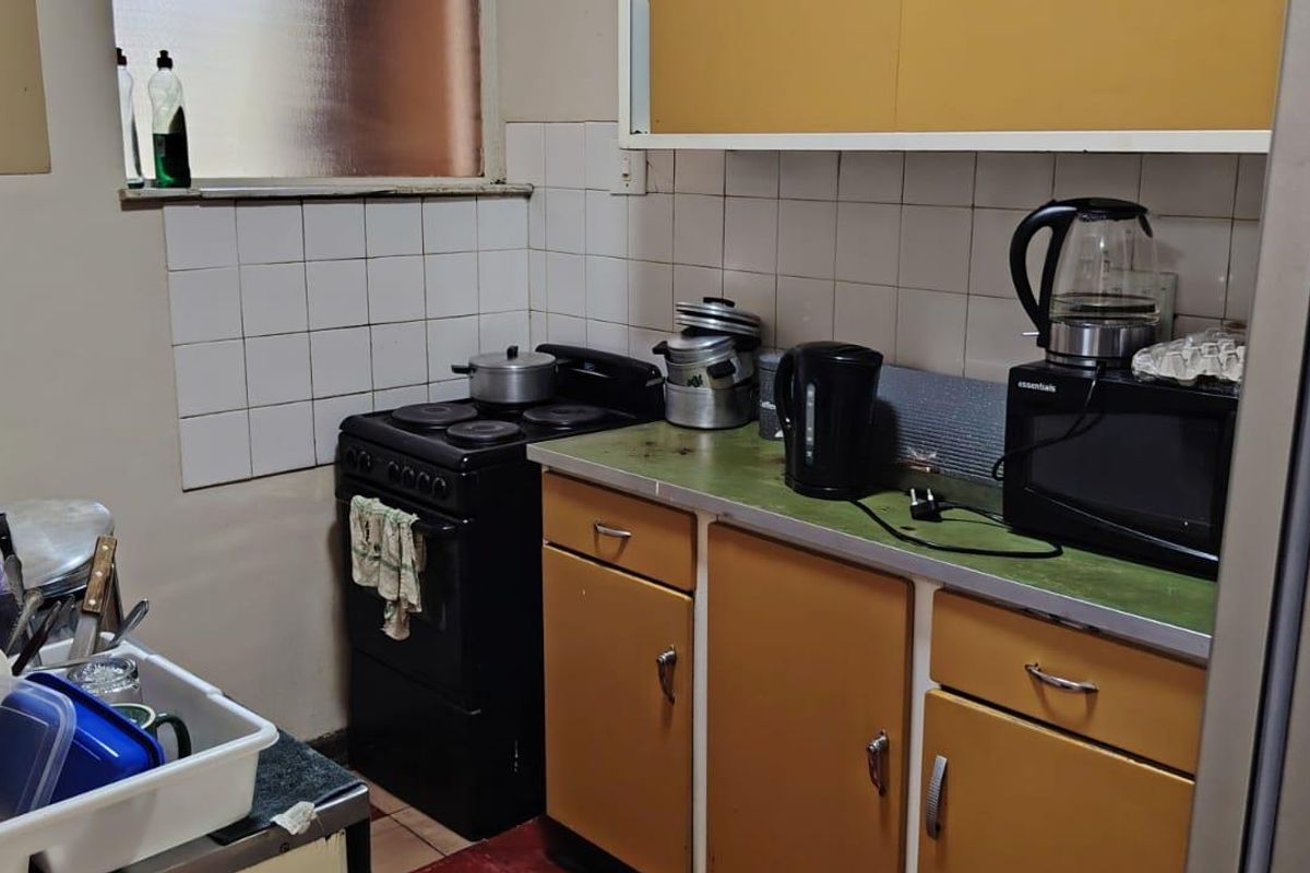 A compact, dated kitchen featuring original cabinetry, a tiled splashback, and a freestanding stove, offering significant potential for modernization and renovation.