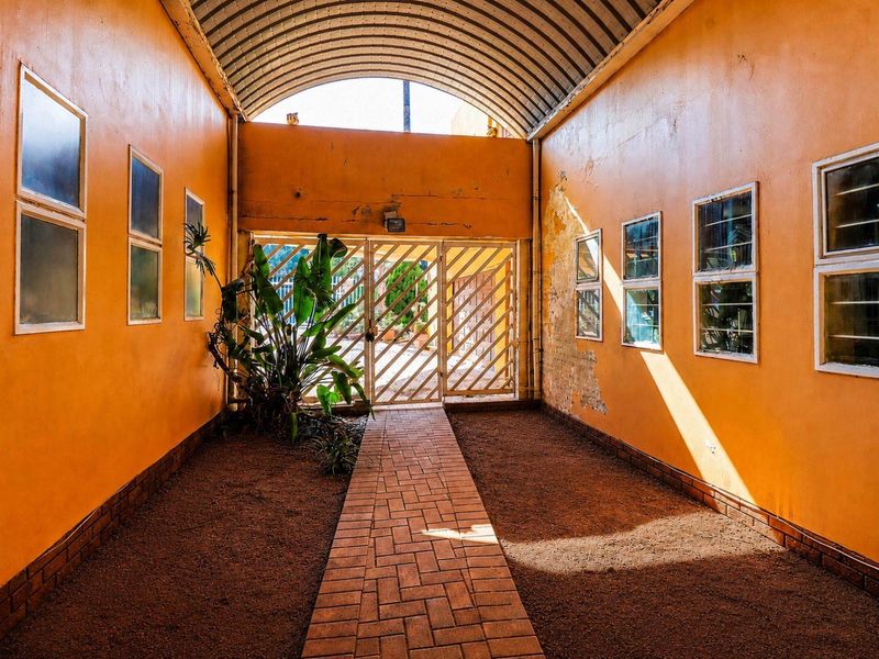 A covered outdoor walkway featuring a barrel vault roof, brick paving, and metal security gate, requiring maintenance to the wall finishes.