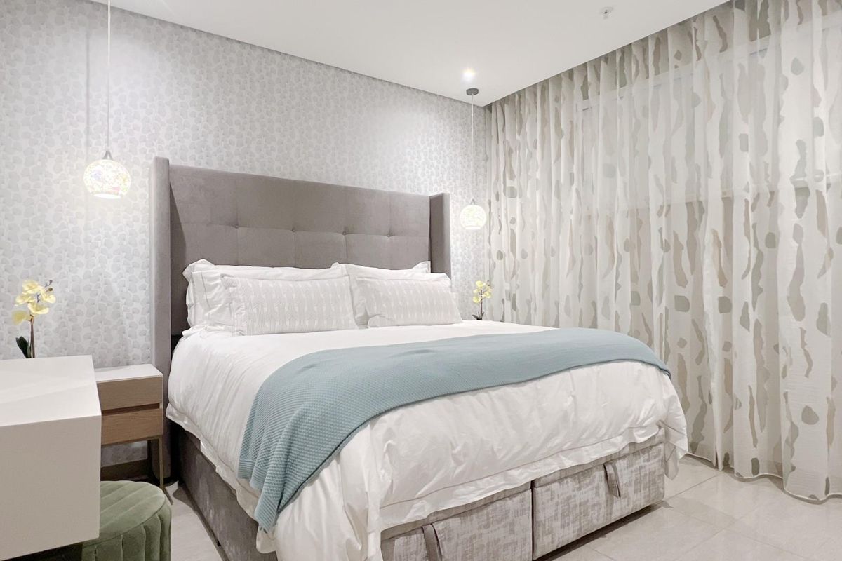 A well-appointed bedroom featuring modern recessed ceiling lighting, patterned wallpaper, and floor-to-ceiling window treatments.