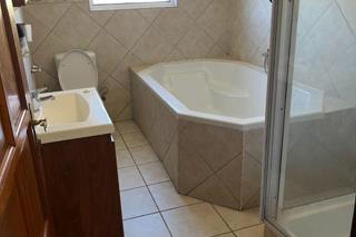 A functional bathroom featuring a built-in corner bathtub, a separate shower enclosure, a vanity basin, and a toilet with neutral wall and floor tiling.